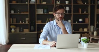 Düşünceli genç işadamı dizüstü bilgisayar kullanarak istatistik raporu üzerinde çalışıyor.