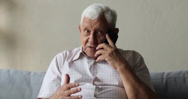 Yaşlı adam koltukta oturup cep telefonuyla konuşuyor.