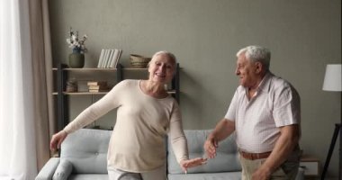 Kaygısız sağlıklı emekliler eşleri oturma odasında el ele tutuşup dans ediyorlar.