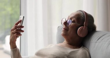 Yaşlı kadın elinde cep telefonu kulaklık takıyor müzik dinliyor.