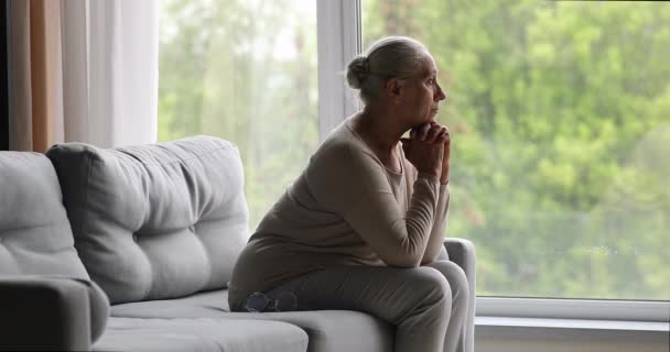 Femme âgée solitaire s'assoit sur le canapé en regardant dans la distance — Video