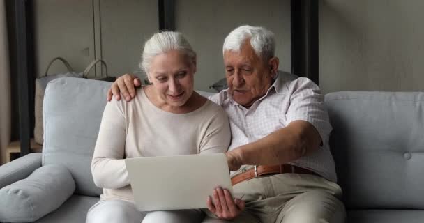 Oudere paar zitten op de bank met laptop leren nieuwe toepassing — Stockvideo