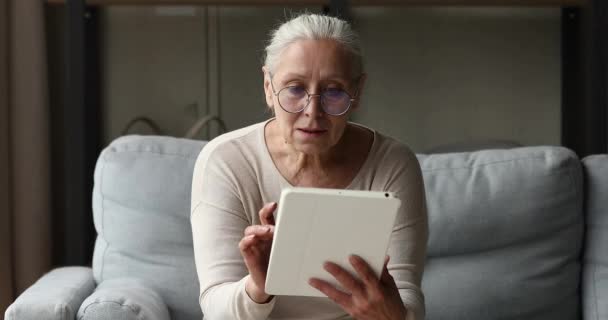 Пожилая женщина с цифровым планшетом выбирает товары, покупает электронные услуги — стоковое видео