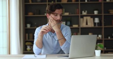 Dizüstü bilgisayarla çok çalışan yorgun genç adam. Gözlükleri çıkar. Gözlerini ovala.