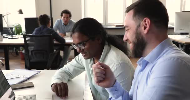В коворкинге мультиэтнические сотрудники сидят за столом и обсуждают онлайн-задачу — стоковое видео