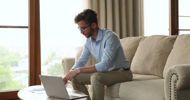 Сосредоточенный бизнесмен тысячелетия платить налоги онлайн с помощью ноутбука на дому — стоковое видео