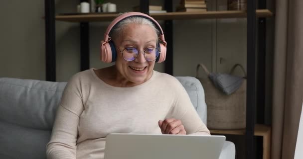 Abuela en auriculares mira portátil hablando en la aplicación de videoconferencia — Vídeo de stock