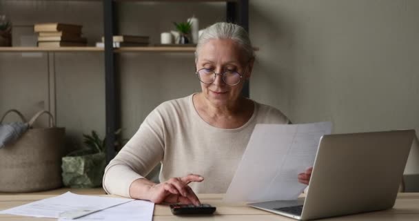 Femme plus âgée calcule le montant sur la calculatrice utiliser des factures de paiement d'ordinateur portable — Video