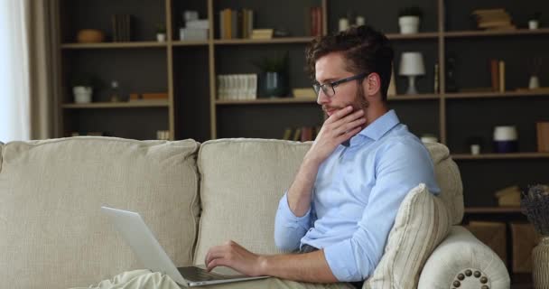 Jovem sentado no sofá fazendo trabalho freelance no laptop — Vídeo de Stock