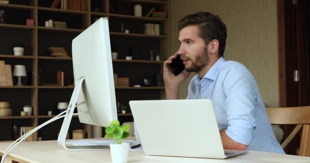 Millennial-Geschäftsmann, der vom Home Office aus arbeitet, berät Anrufer per Telefon — Stockvideo