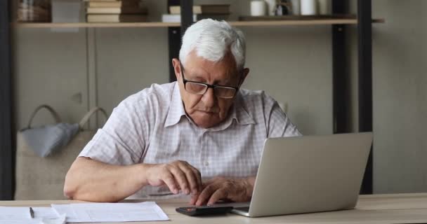 Hombre mayor serio usando calculadora y portátil hace pagos en línea — Vídeos de Stock