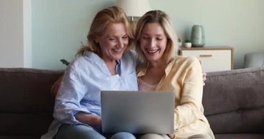 Mutlu büyük anne yetişkin kız kanepede dizüstü bilgisayarla oturuyor.