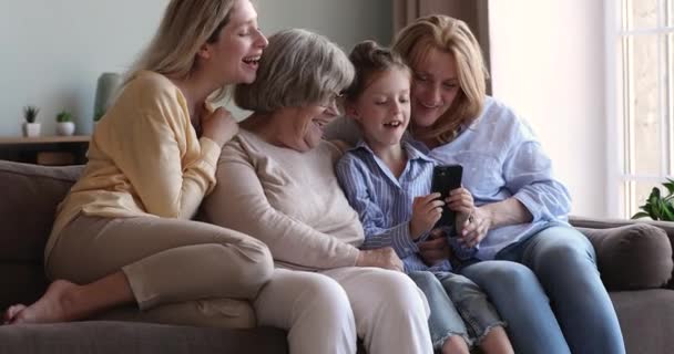 Mulheres multigeracionais família sentar no sofá se divertindo usando smartphone — Vídeo de Stock