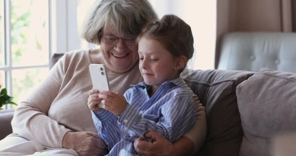 Vieille mamie son arrière-petite-fille s'asseoir sur le canapé en utilisant un smartphone — Video