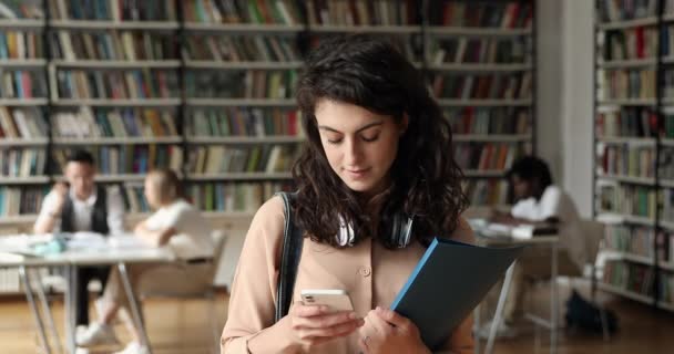 Ung latinsk kvinna student som använder mobiltelefon i college bibliotek — Stockvideo