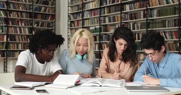 Cuatro becarios multiculturales serios que se dedican al papeleo en la biblioteca — Vídeo de stock