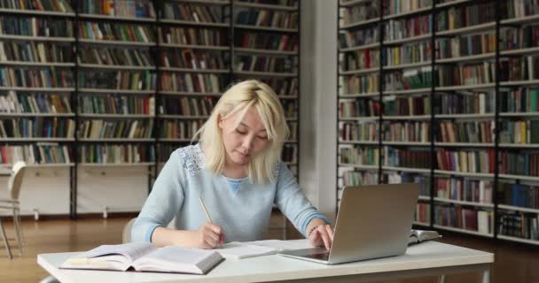 Mladá asijská žena studie na dálku v knihovně pomocí notebooku — Stock video