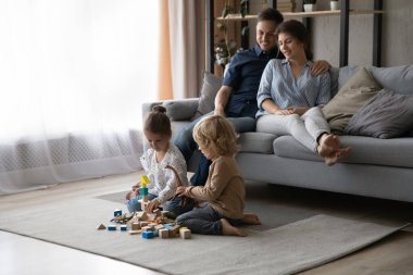 Rahat genç ebeveynler evde oynayan küçük çocukları izliyorlar..