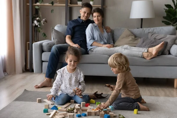 Liebevolle Eltern sitzen auf dem Sofa, während kleine Kinder Spielzeug spielen. — Stockfoto