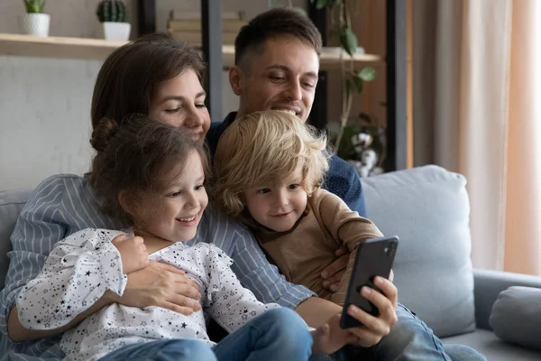 Счастливые молодые родители и маленькие дети с помощью мобильного телефона. — стоковое фото