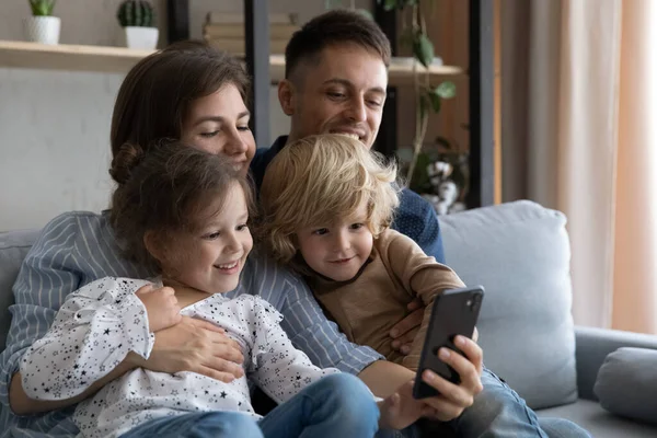 Mutlu genç ebeveynler ve küçük çocuklar cep telefonu kullanıyor..