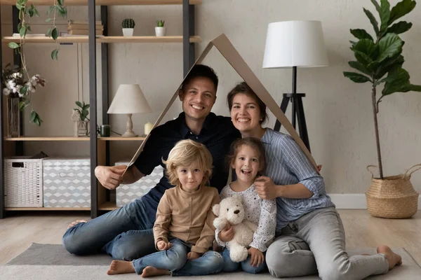 Portrait of smiling family sitting under carton roof. — Stock Photo, Image