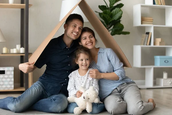 Dreamy happy family sitting on floor under carton roof. — Stock Photo, Image