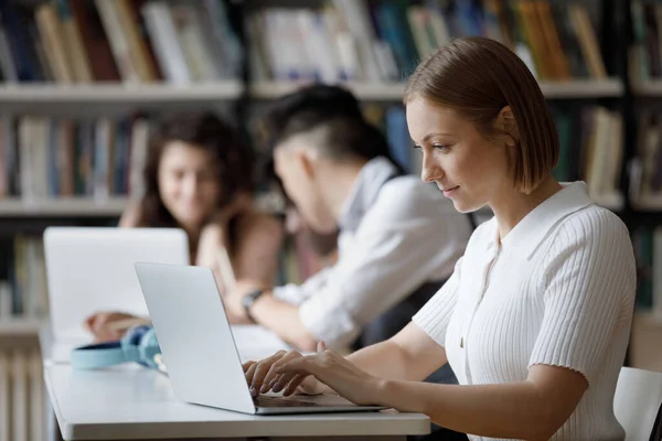 Heureuse étudiante intelligente concentrée travaillant sur ordinateur dans la bibliothèque. — Photo