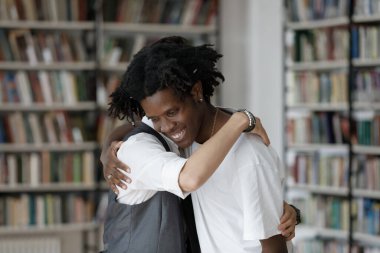 Mutlu genç adam gülümseyen Afrikalı Amerikalı arkadaşına sarılıyor..