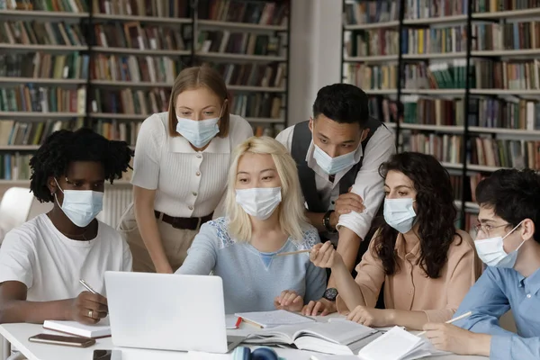 Group of happy multiethnic students in facemasks studying in library. — Stock Photo, Image