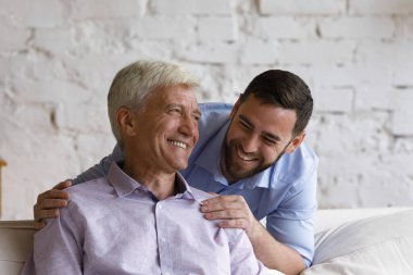 Mutlu, yakışıklı, yetişkin oğlu yaşlı babasına sarılıyor.