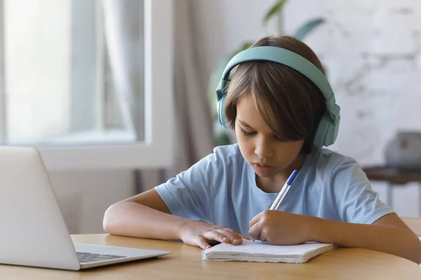 Schooljongen dragen koptelefoon luisteren audio, doen huiswerk thuis — Stockfoto