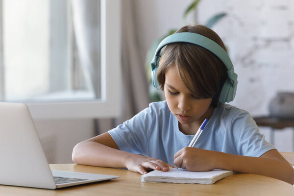 Schoolboy wear headphones listen audio, do homework at home