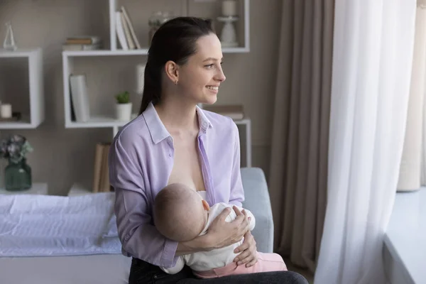 Happy dreamy young mother feeding baby milk from breast — Stock Photo, Image