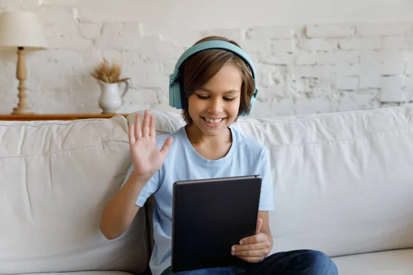 Jongen dragen draadloze hoofdtelefoon start videocall gesprek gebruik maken van digitale tablet — Stockfoto