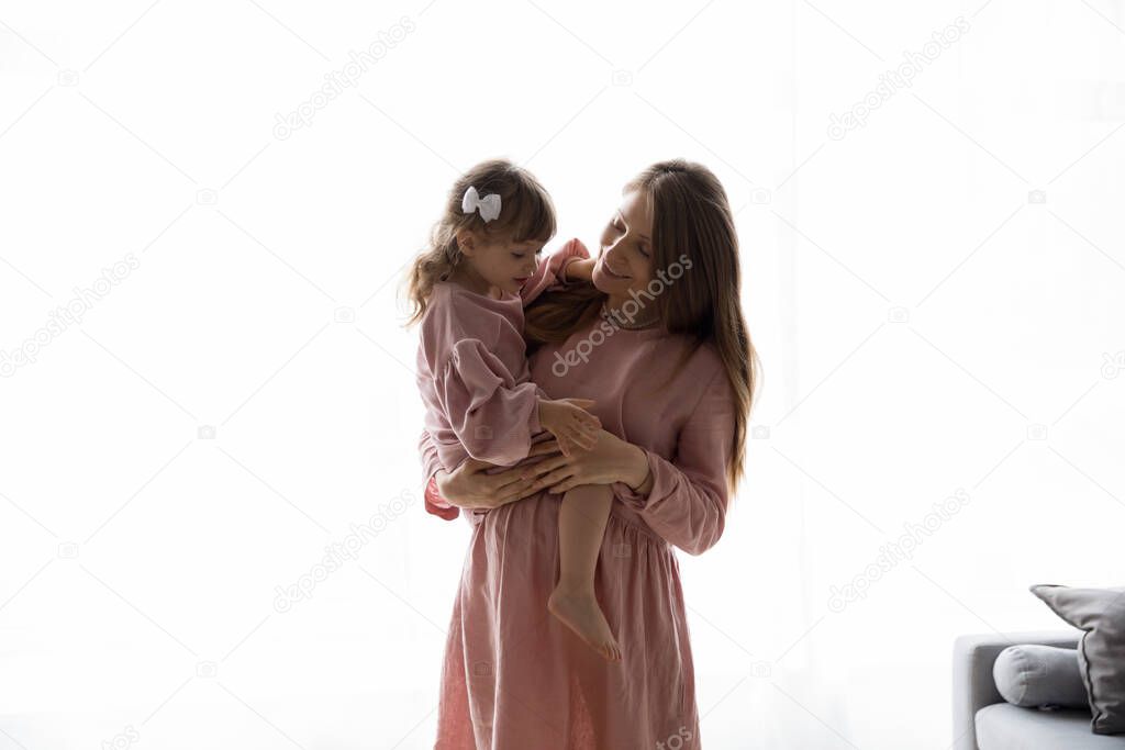 Happy pregnant mom holding elder little daughter girl in arms