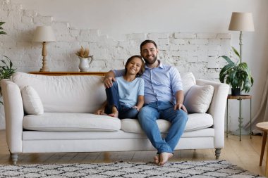 Küçük çocuk, genç baba kanepeye otur ve kameraya bak.