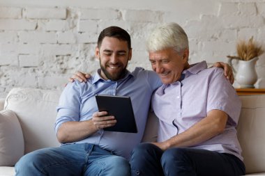 Mutlu yaşlı adam genç yetişkin oğlu dijital tablet kullanıyor.