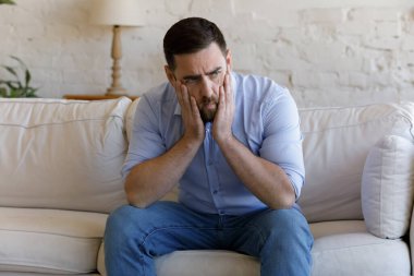 Man sit on sofa looks depressed, thinking on problems clipart