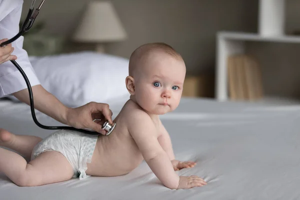 Serious baby patient examined by pediatrician on double bed at home — Stock Photo, Image