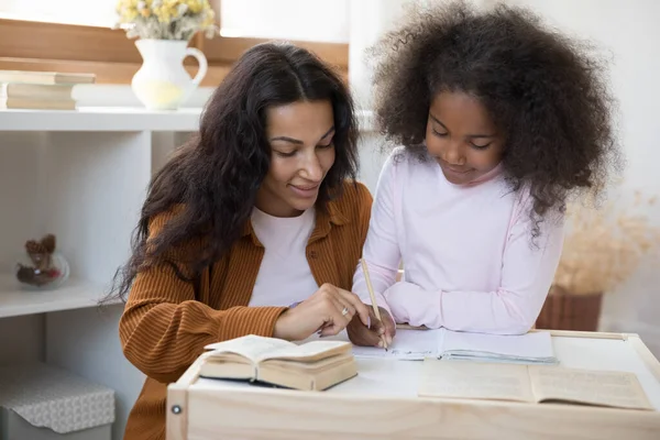 Zorgen voor jonge Afro-Amerikaanse moeder helpen klein kind met huiswerk. — Stockfoto