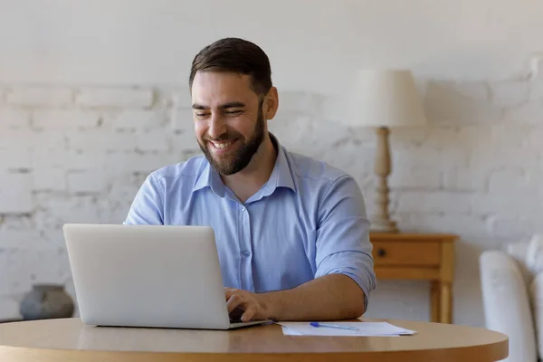 Młody przystojny freelancer człowiek siedzieć przy stół za pomocą laptop — Zdjęcie stockowe