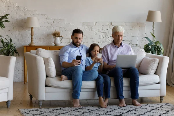 Tiga generasi keluarga duduk di sofa menggunakan beragam gadget modern — Stok Foto