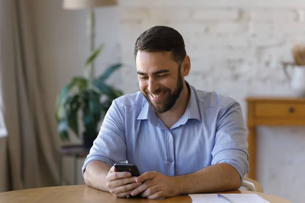 Empresario se sienta en la mesa mantenga el teléfono inteligente disfrutar de chat en línea —  Fotos de Stock