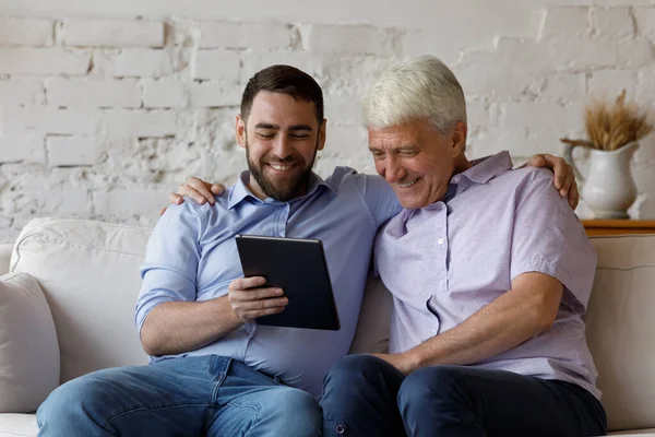 Boldog idősebb férfi fiatal felnőtt fia digitális táblagépet használ — Stock Fotó