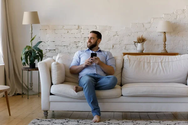 Man duduk di sofa dengan smartphone tampak ke jarak — Stok Foto