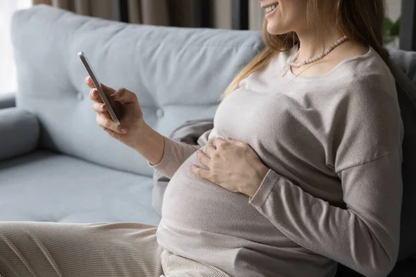 Feliz joven embarazada madre usando el teléfono celular, relajarse en el sofá cómodo — Foto de Stock