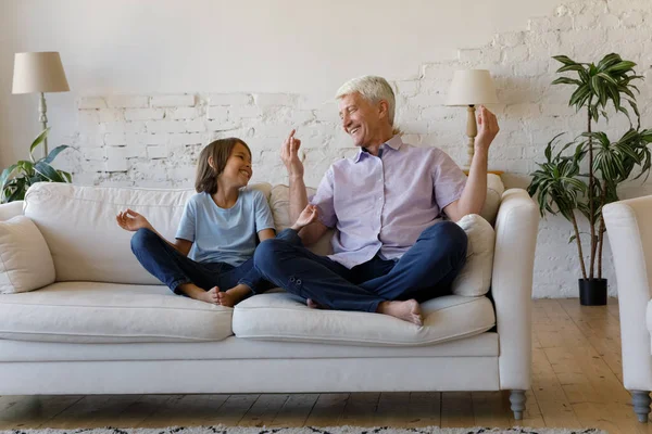 Maduro abuelo y pequeño nieto riendo sentado piernas cruzadas en el sofá — Foto de Stock