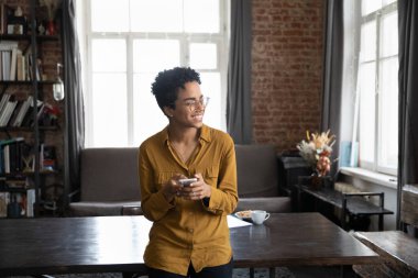 Mutlu, hayalperest, akıllı telefon kullanan, ofisteki geniş çalışma masasında duran, pencereden uzaklara bakan, iyi haberleri düşünen, internette sohbet eden, düşüncelerine gülümseyen, serbest çalışan bir kadın.