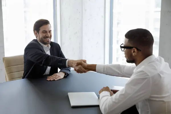 Feliz Joven Candidato Vacante Masculina Estrechando Mano Con Gerente Afroamericano Imágenes De Stock Sin Royalties Gratis